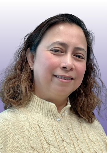 Smiling person in cream sweater against purple background.